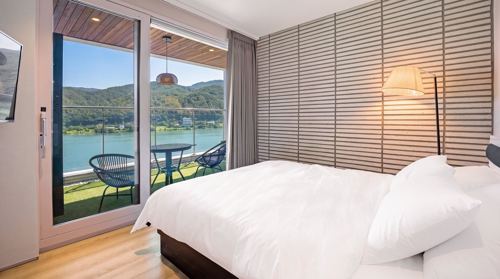 A bedroom with a large bed, a view of a lake, and a balcony with chairs.
