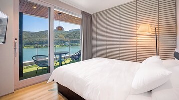 Un dormitorio con una cama grande, vistas a un lago y un balcón con sillas.