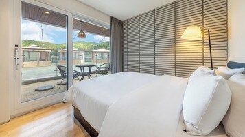Un dormitorio con una cama grande, vistas a un patio exterior con mesas y sillas, y una lámpara en la mesita de noche.