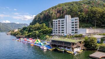 Un hotel frente al agua con zona de piscina, barcos y una ladera cubierta de bosque.