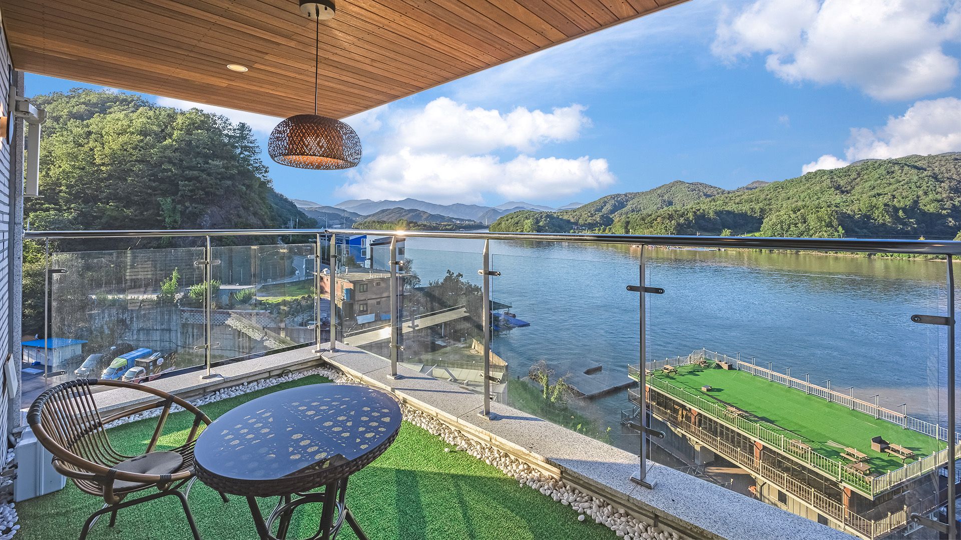 A balcony with a table and chairs, overlooking a river and green hills.