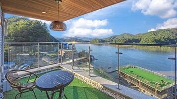 A balcony with a table and chairs, overlooking a river and green hills.