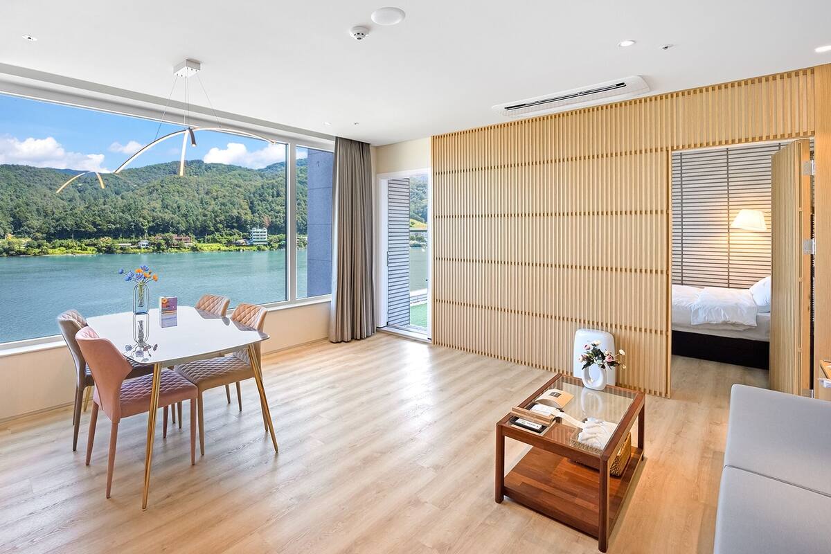 Ein modernes Hotelzimmer mit großem Fenster und schöner Aussicht auf See und Wald.