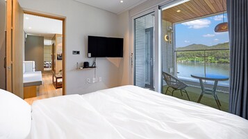 Et hotelværelse med seng, fjernsyn, udsigt til en sø og en balkon med bord og stol.