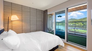 Un dormitorio con cama, lámpara y vista a un lago a través de una puerta corrediza de vidrio.