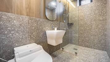 A modern bathroom with a white sink, a glass shower enclosure, and a toilet.