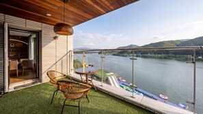 A balcony with a view of a river and mountains, furnished with wicker chairs and a table, and a glass railing. - Gapyeong Laputa Resort (Gapyeong)