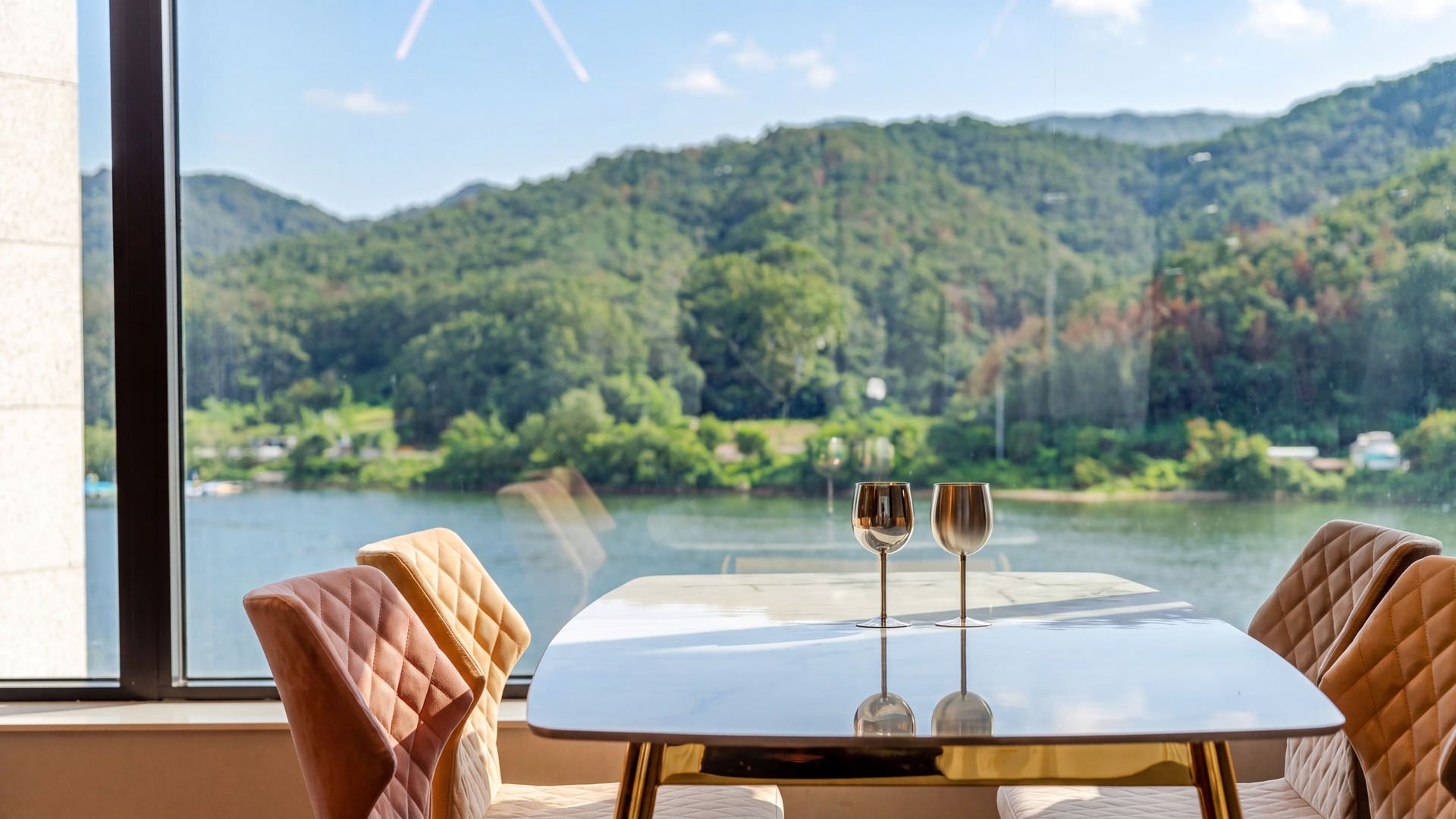 A table with two wine glasses and a view of a lake and mountains.