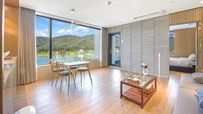 Una habitación de hotel moderna con comedor, un ventanal con vista a un lago y montañas, y una cama orientada a la habitación.