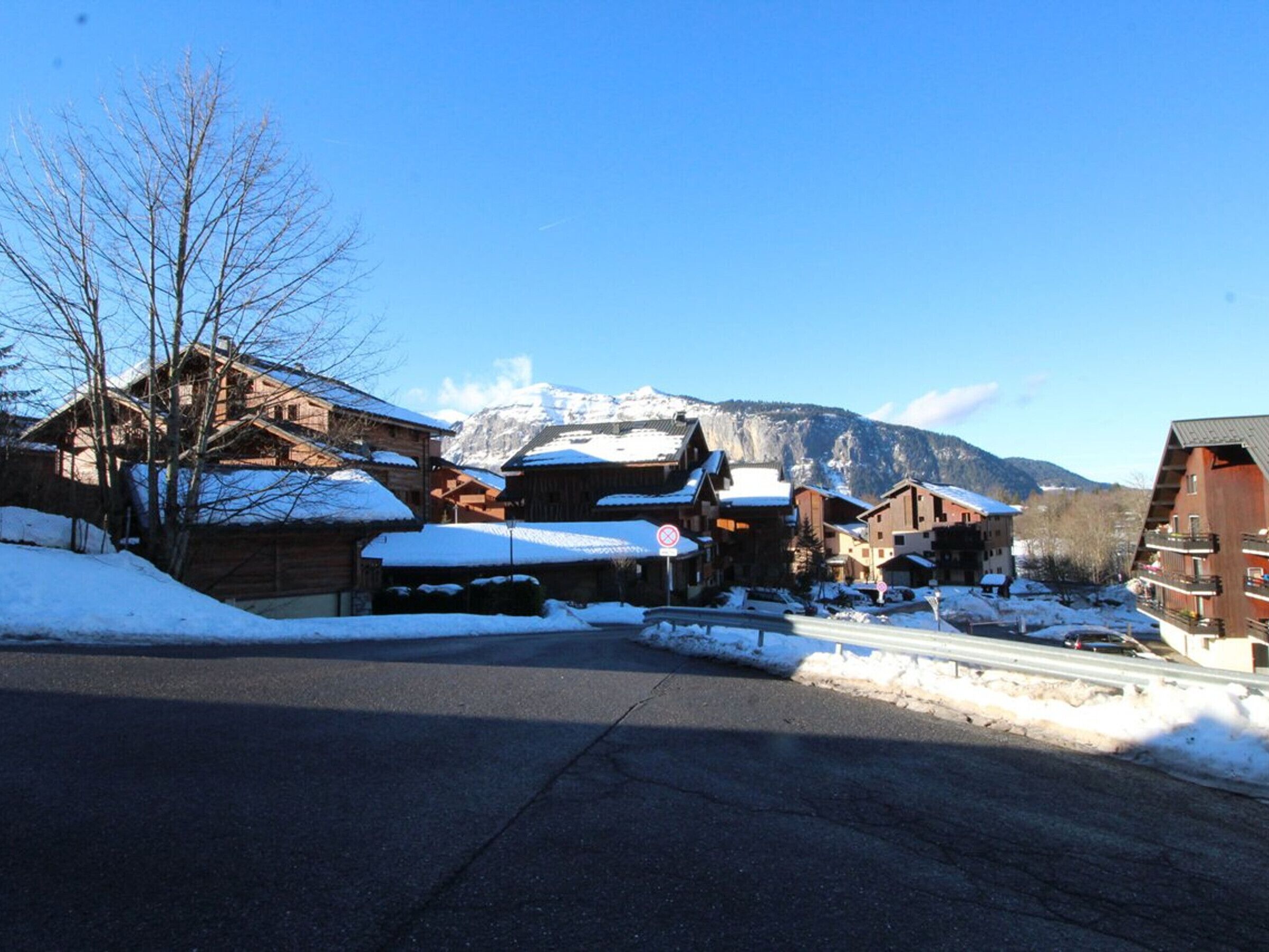 A snow-covered village with wooden buildings, a clear sky, and mountains in the background.