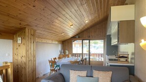 Un acogedor interior de cabaña con techo de madera, un comedor con mesa y sillas, y una kitchenette.