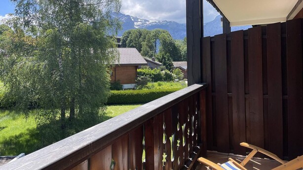 Un balcón de madera con vistas a una cordillera y una casa al fondo.