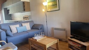 Una sala de estar con un sofá, una mesa de centro de madera, un televisor y una estantería.