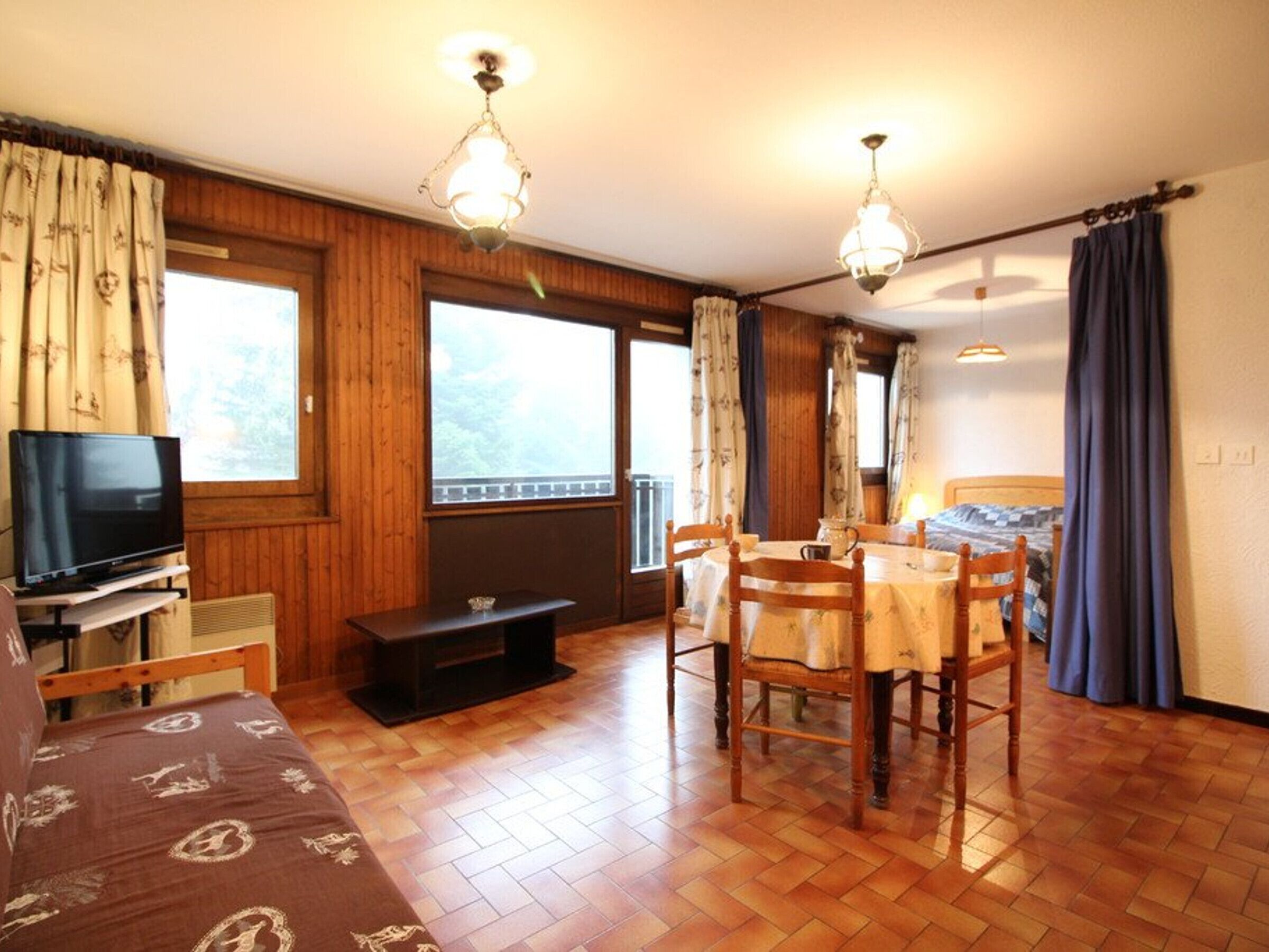 Ein gemütliches Zimmer mit Holzböden, einem Fernseher, einem Esstisch mit Stühlen und großen Fenstern.