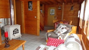 A cozy cabin interior with a wooden interior, a small white stove, a dining area with a table and chairs, and a sofa with patterned cushions.