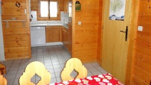 A wooden interior with a kitchen area, a dining table with chairs, and a door with a map.