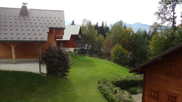 A wooden cabin with a sloped roof, surrounded by a well-maintained lawn and dense forest.