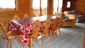 A wooden dining area with a table covered in a red and white patterned tablecloth, surrounded by wooden chairs.
