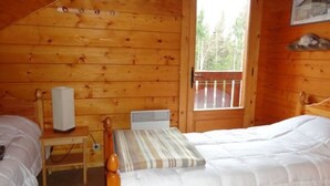 A wooden cabin room with two beds, a small table, and a window.
