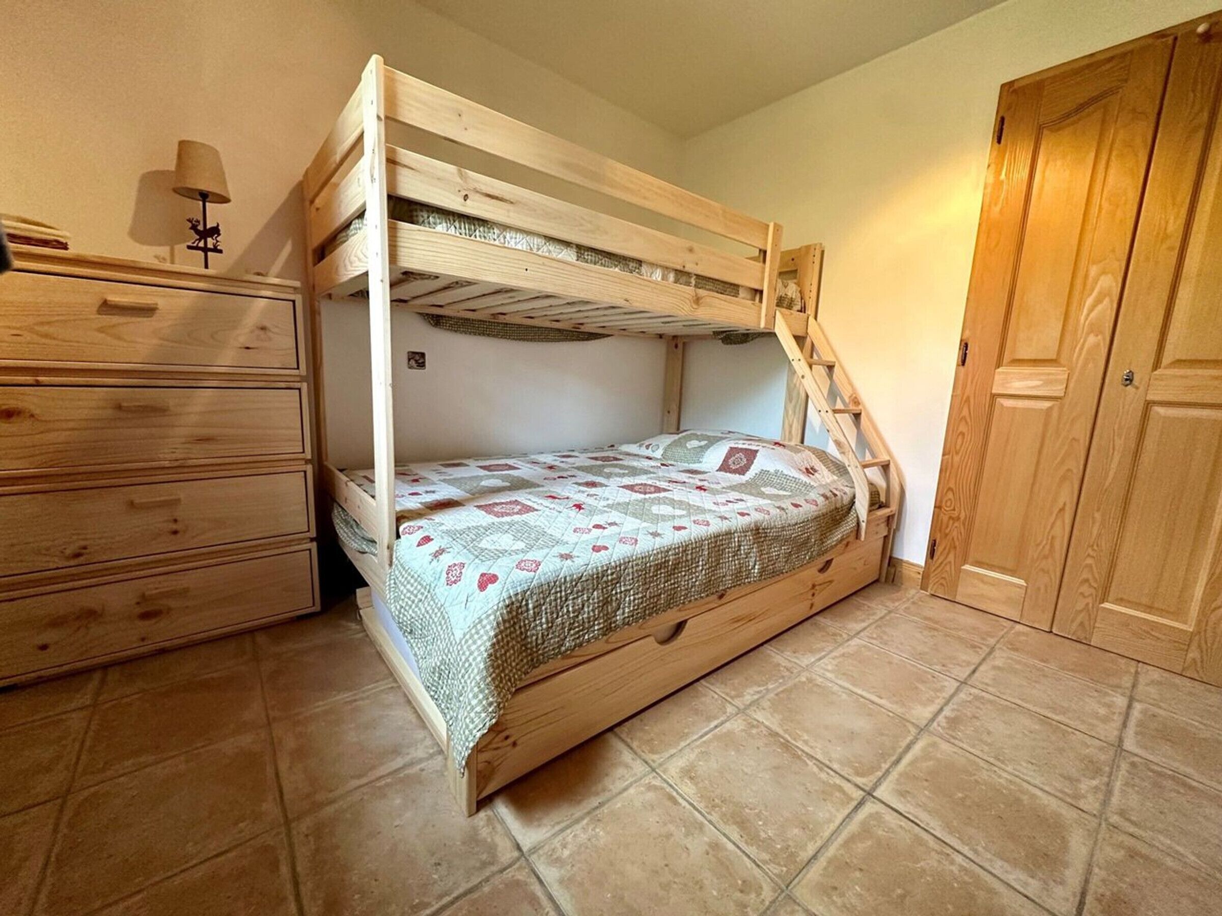 Een stapelbed met houten frame, een dressoir met lades en een deur.