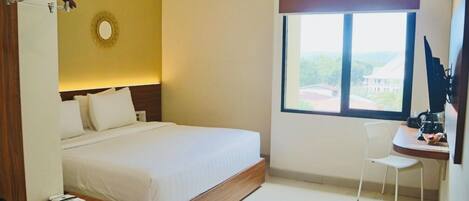 A hotel room with a bed, a desk with a chair, a window with a view, and a small trash bin.