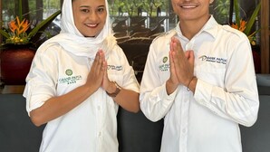 Two individuals in white shirts with the Grand Papua Sentai logo, standing in front of a marble wall with the hotel's name.