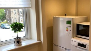 Eine kompakte Küche mit Kühlschrank, Mikrowelle und Geschirrspüler. Auf der Fensterbank steht ein kleiner Topfpflanze.
