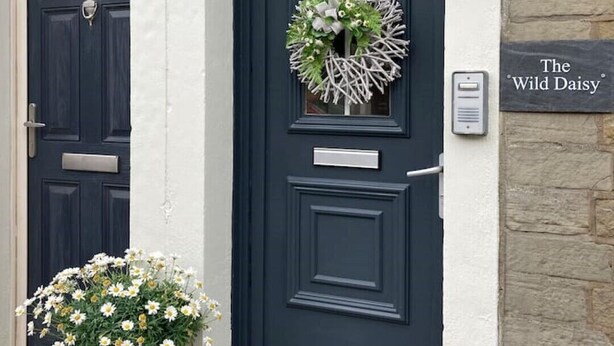 Eine dunkelblaue Tür mit einem Kranz und einem Schild, auf dem "The Wild Daisy" steht.