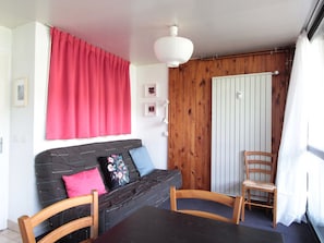 Um quarto aconchegante com um sofá preto, uma cadeira de madeira, uma mesa de jantar e um guarda-roupa de madeira.