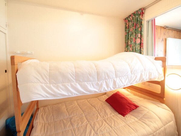 A single bed with a wooden frame, a beige quilt, and a white pillow.