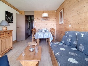 A cozy cabin interior with a dining area, a sofa, and a wooden table with glasses. - Renovated apartment at the foot of the slopes with balcony (Les Menuires)