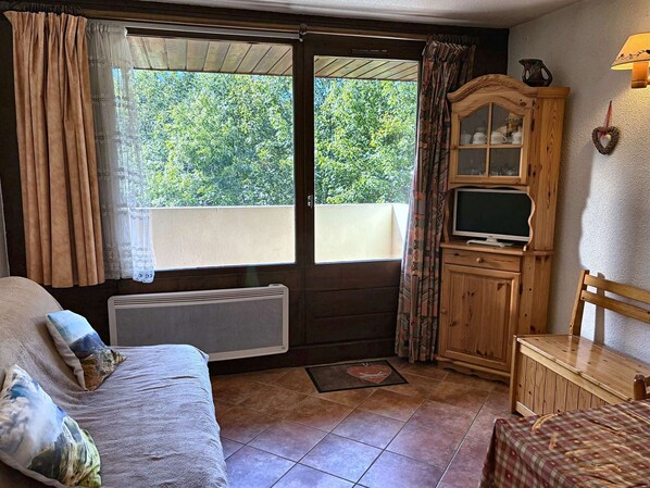 A cozy room with a bed, a wooden cabinet with a television, and a window with curtains.