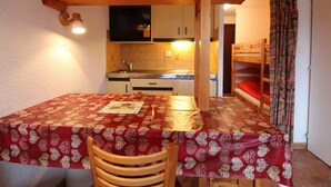 Une pièce de taille modeste comprenant une table à manger, une chaise, un lit superposé, un coin cuisine et une salle de bain.