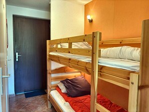 A bunk bed with a wooden frame and white bedding, a door with a handle, and a wall-mounted light fixture.