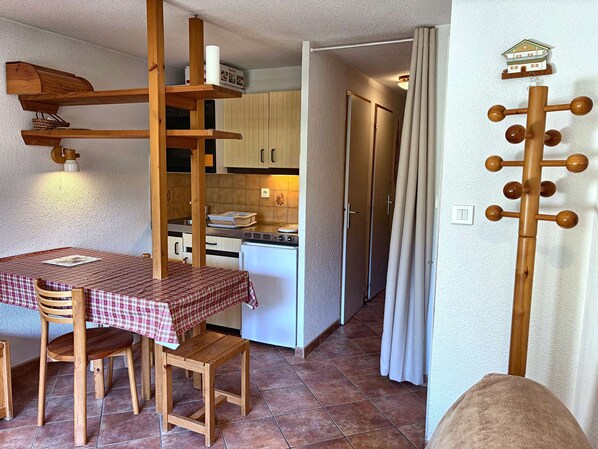 A compact kitchen with a dining area, wooden furniture, and a curtain rod.