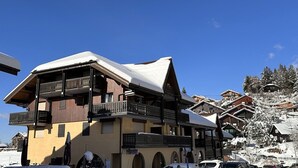 A multi-story chalet with balconies, a ski slope in the background, and a clear blue sky. - Studio for 4 at the foot of the slopes, balcony, ski locker, TV (Les Carroz d'Arâches)