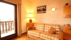 A cozy living room with a checkered sofa, a lamp, a painting, and a view through a large window. - Studio for 4 at the foot of the slopes, balcony, ski locker, TV (Les Carroz d'Arâches)