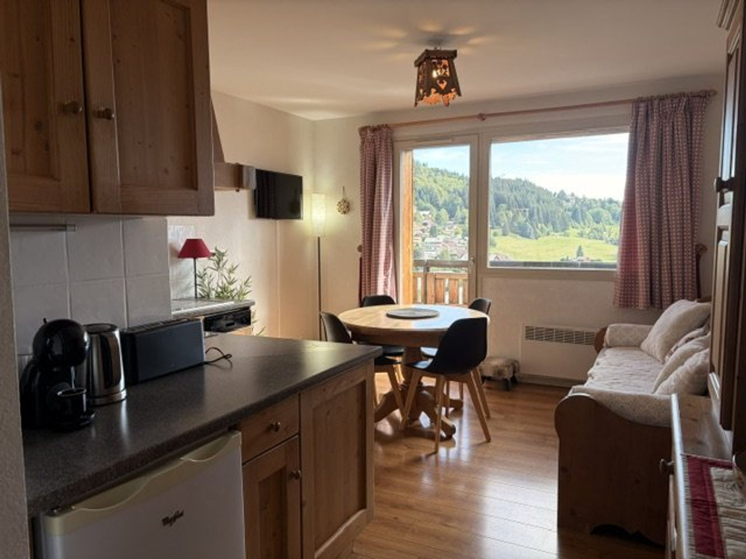 A kitchen with wooden cabinets, a dining table with chairs, a sofa, and a window with curtains.