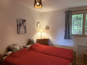 Un dormitorio con dos camas, una mesita de noche con lámpara, un espejo, una ventana con cortinas y una obra de arte colgada en la pared.