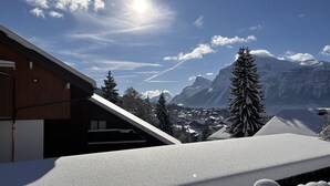 Un edificio moderno con techo inclinado, rodeado de montañas y árboles cubiertos de nieve.