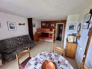 A cozy room with a bunk bed, a sofa, a dining table, and various wall decorations.