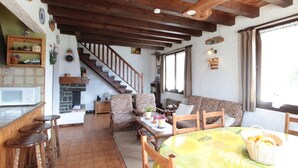 A cozy living room with a wooden staircase, a dining area with a table and chairs, and a kitchen with a microwave. - Cozy Chalet 6p, 2BR, Near Ski Lifts, Garage, South-West Terrace (Arâches-la-Frasse)