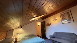 Makuuhuoneessa on sänky, sohva, puinen katto ja ovi.