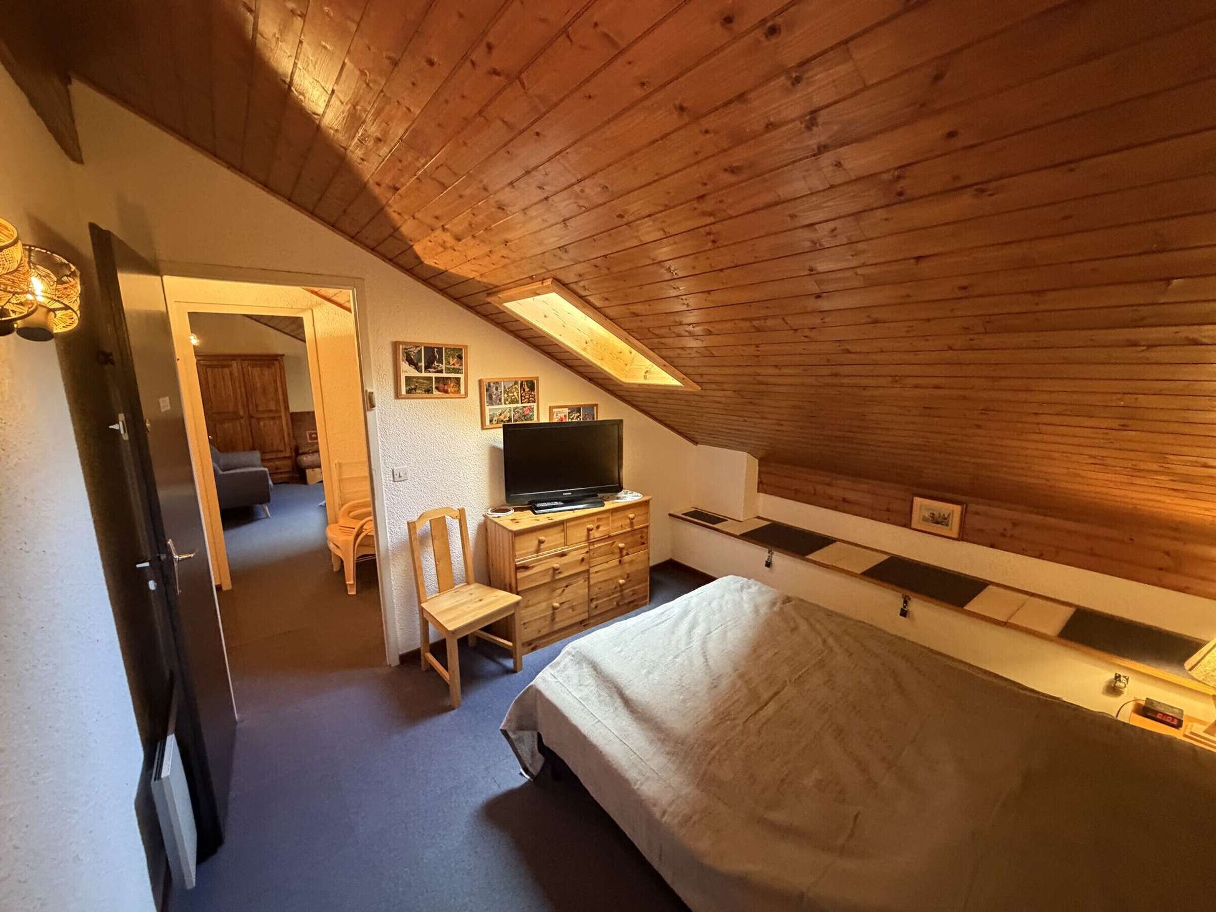 Une chambre avec un plafond en pente, des murs en bois, un lit, une commode, un téléviseur et une chaise.