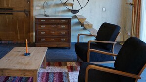 Ett mysigt rum med ett träpanelat tak, en trappa med en unik, hjulinspirerad design, en byrå i trä, två svarta stolar och en färgglad, randig matta.