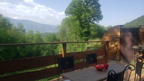 En träveranda med ett bord och stolar, med utsikt över en skogsklädd dal och berg.
