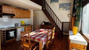 Eine gemütliche Küche mit Holzausbau, einem Esstisch mit kariertem Tischläufer und einer Treppe, die in ein Obergeschoss führt.