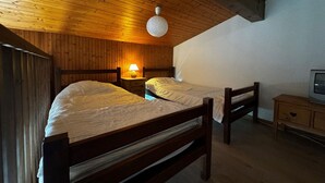 Ein Schlafzimmer mit zwei hölzernen Betten, einem Nachttisch, einer Lampe und einem Fernseher auf einer Holzkommode.