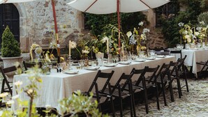 An outdoor dining area with stone walls, tables set with white tablecloths, and floral centerpieces. - Urlaub im Wasserschloss Irmelshausen (Höchheim)