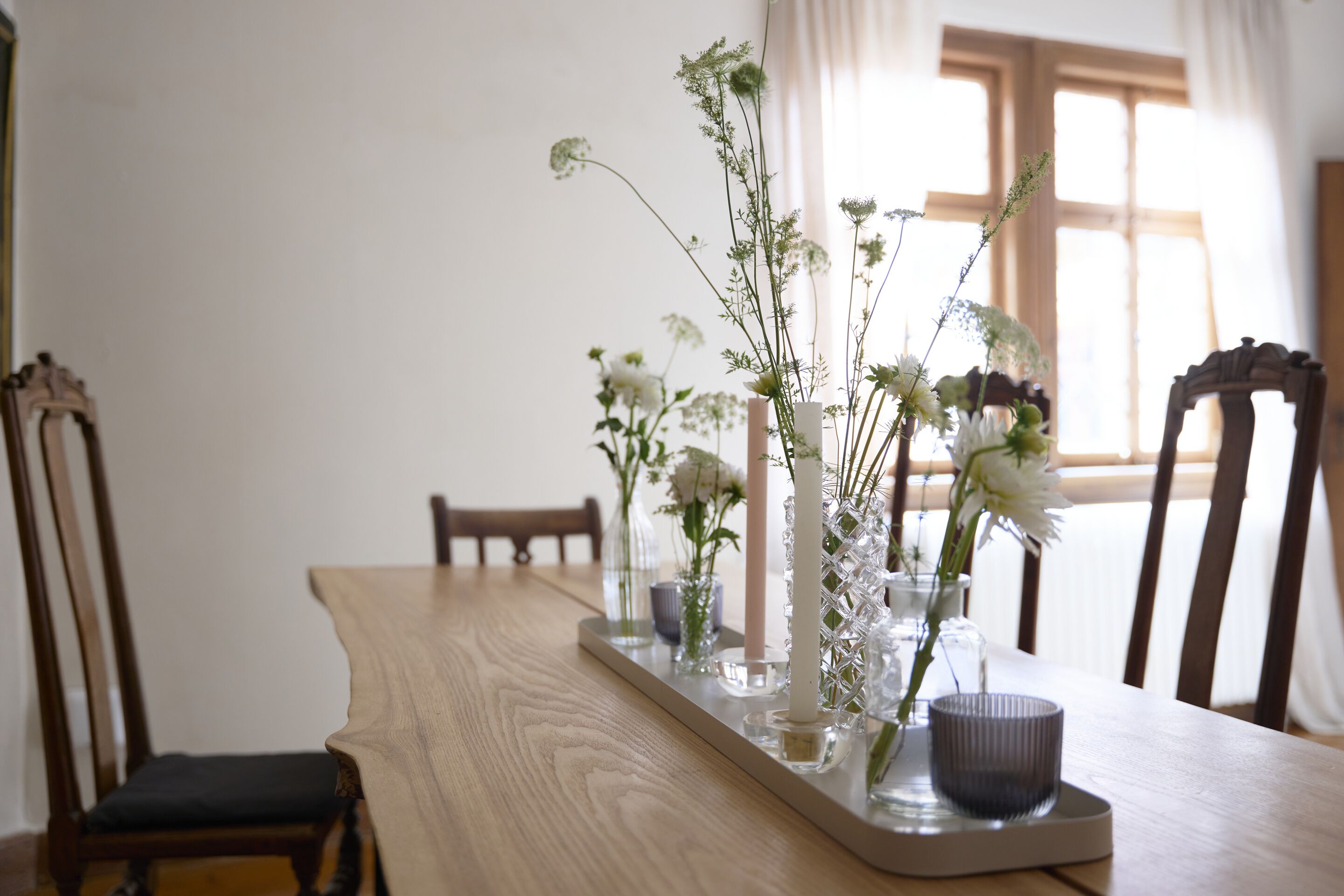 Ein Holztisch mit einer Tablett, auf dem verschiedene Glasvasen mit Blumen stehen.